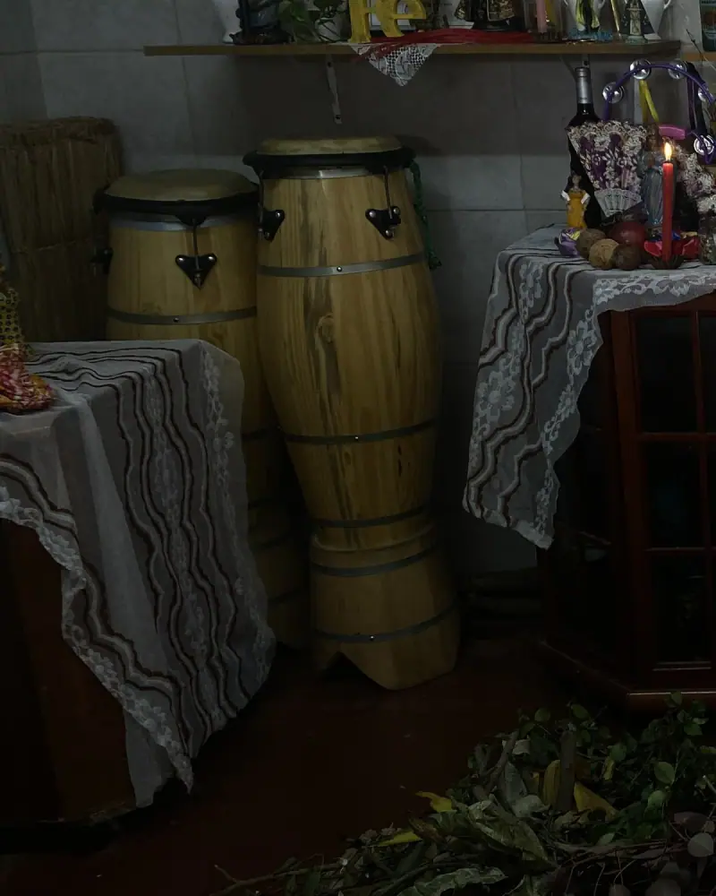 Dois atabaques de madeira ao lado do congá, entre mesas cobertas com toalhas de renda