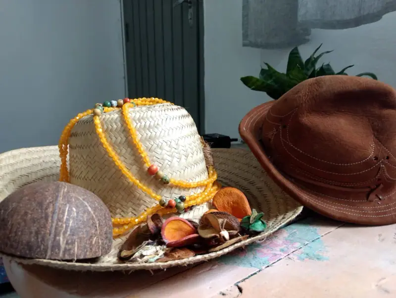 Chapéu de palha com guias de contas amarelas, chapéu de couro e cuia de coco sobre a mesa
