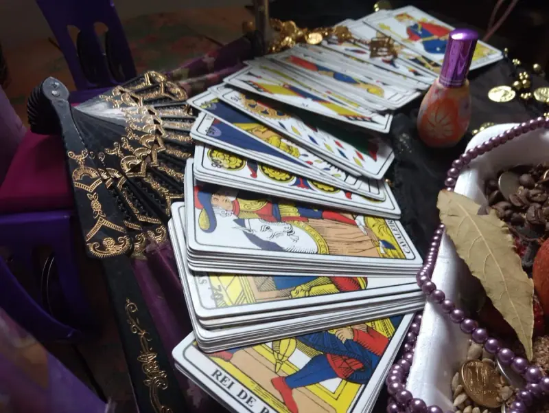 Cartas de tarô abertas em leque sobre a mesa, com leque preto e dourado e colar de pérolas roxas